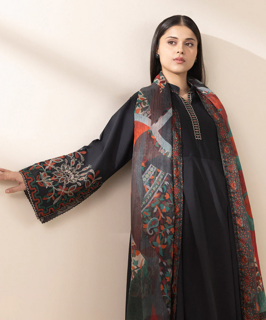 Woman wearing a black outfit with a colorful patterned scarf against a plain background