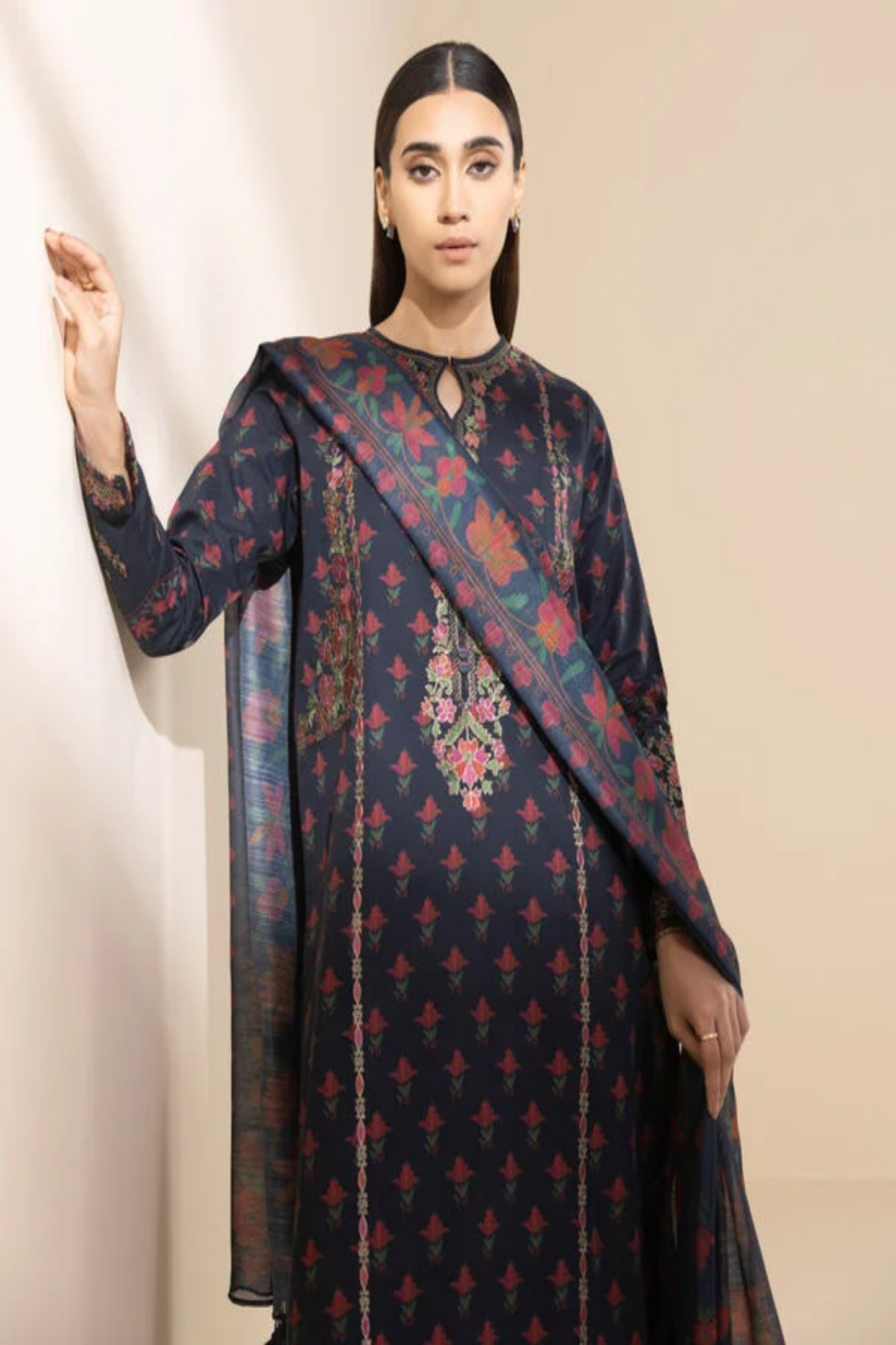 Woman wearing a dark blue traditional outfit with floral patterns on a beige background