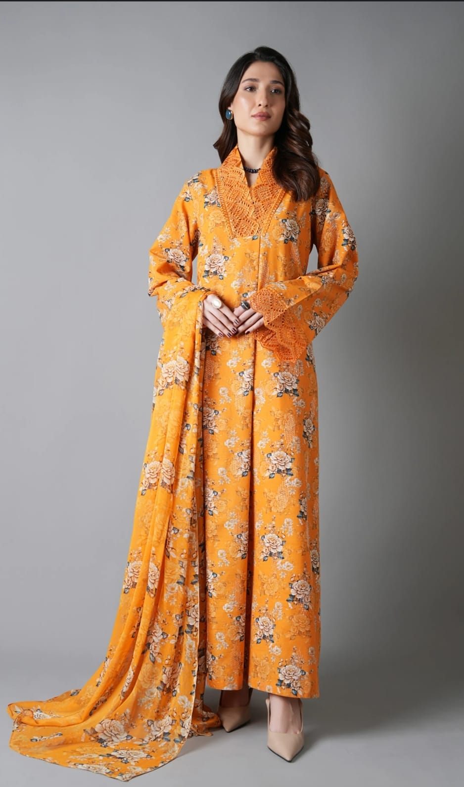 Woman wearing a bright orange traditional outfit with floral patterns on a gray background