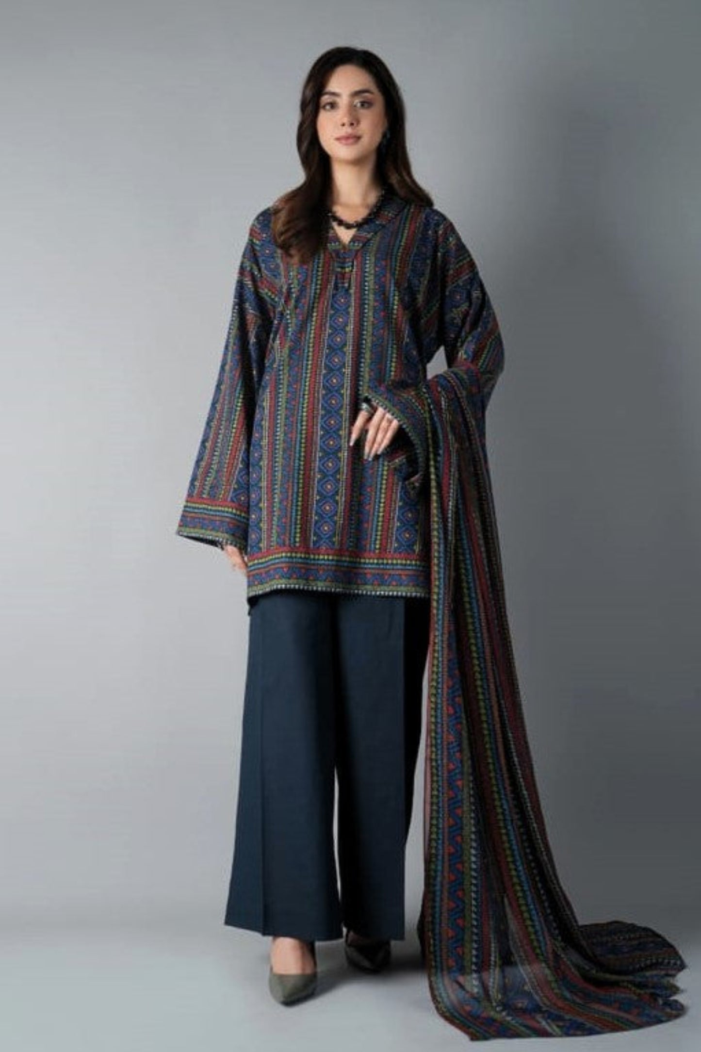 Woman wearing a patterned outfit with a long scarf against a gray background