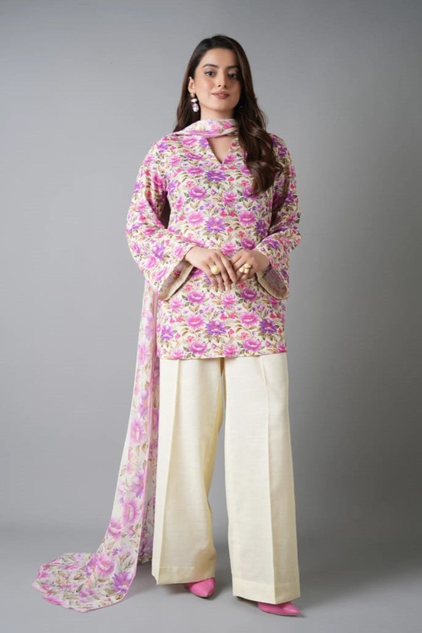 Woman wearing a floral outfit with a pink scarf on a gray background