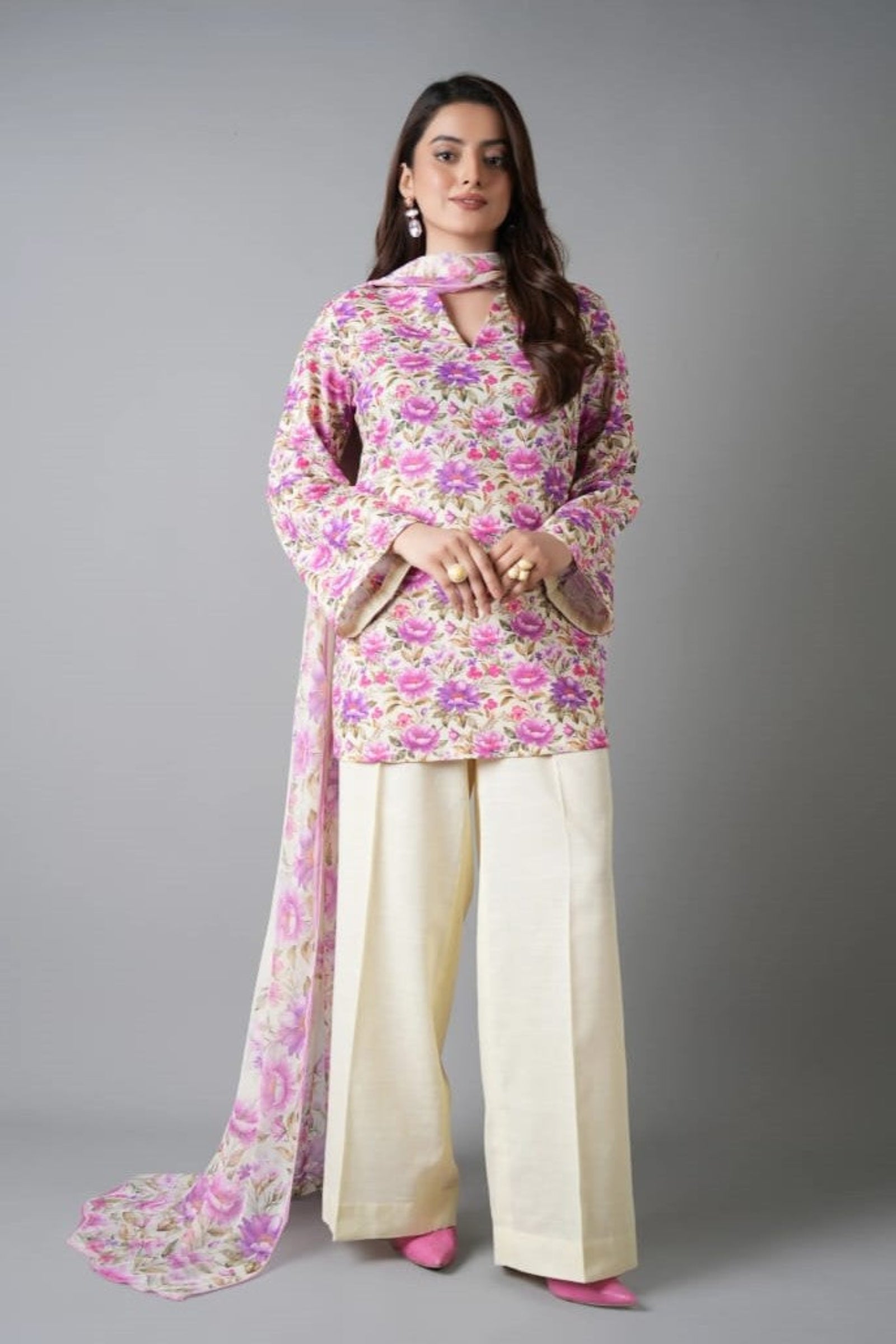 Woman wearing a floral outfit with a pink scarf on a gray background