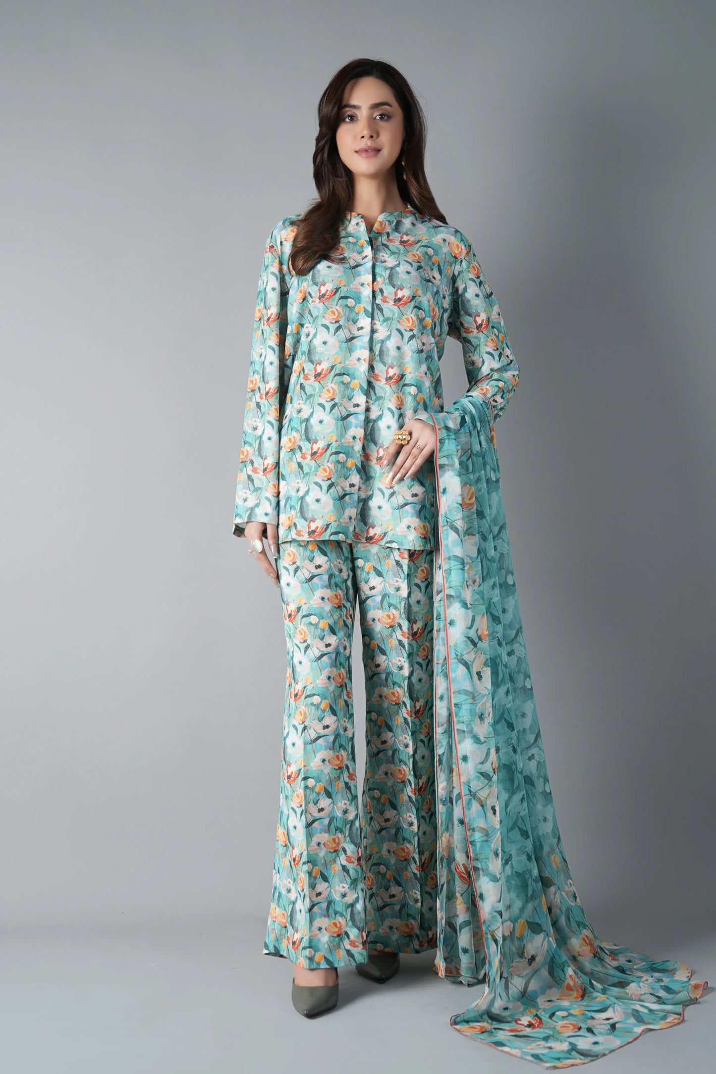 Woman wearing a floral outfit with a long scarf on a gray background