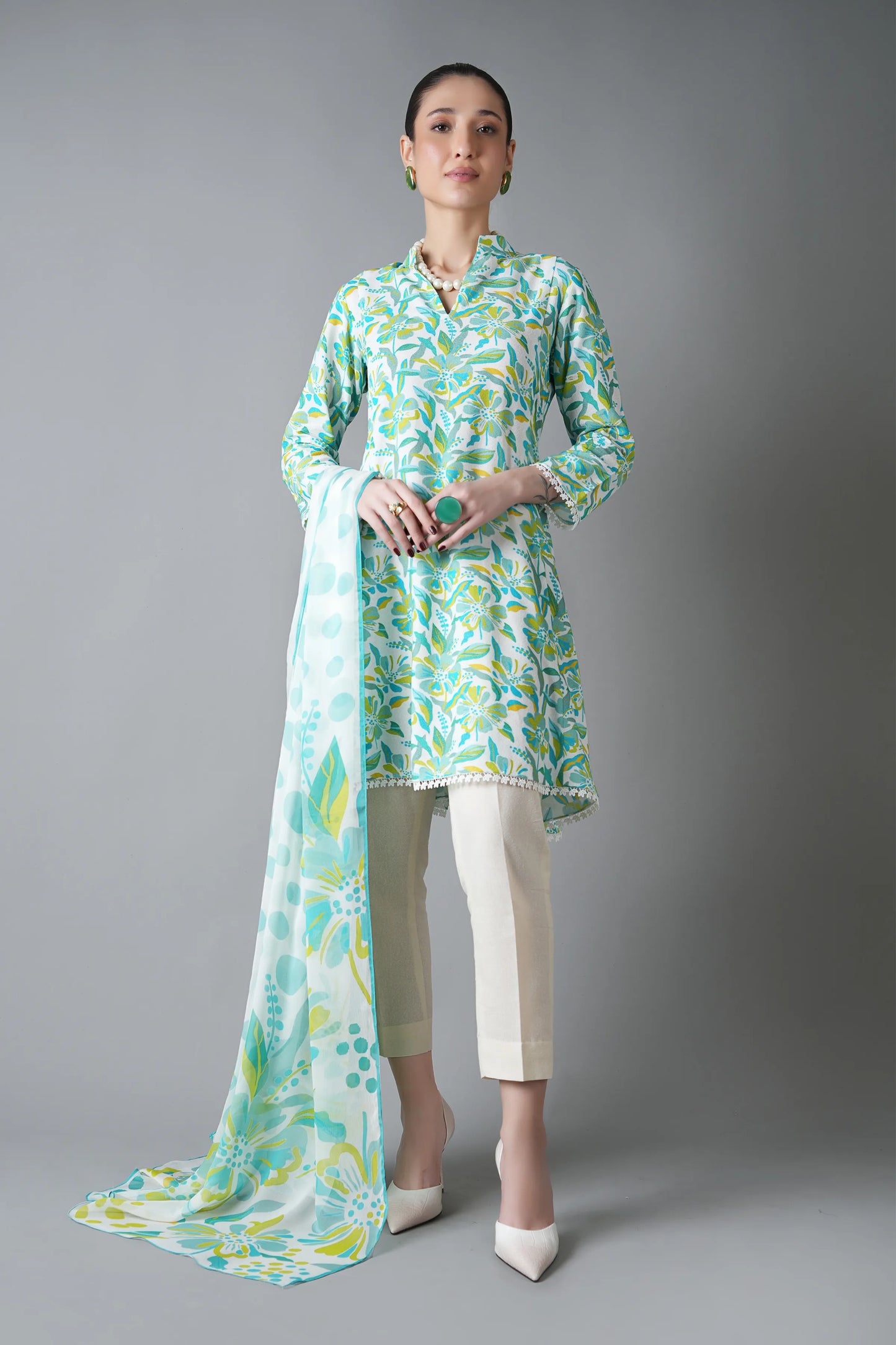 Woman wearing a light green and white patterned outfit with a long scarf on a gray background