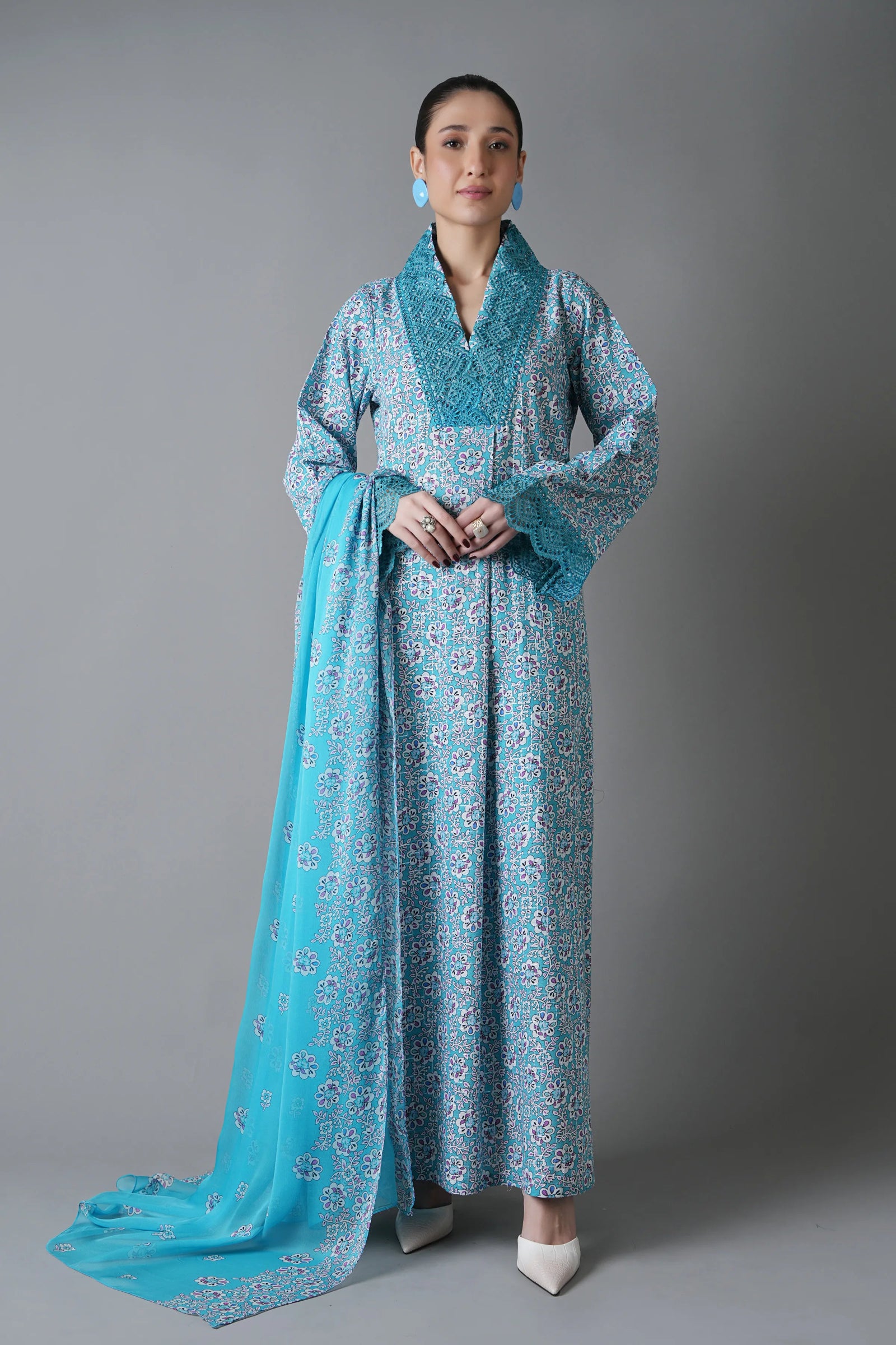 Woman wearing a blue patterned dress with a matching scarf against a gray background