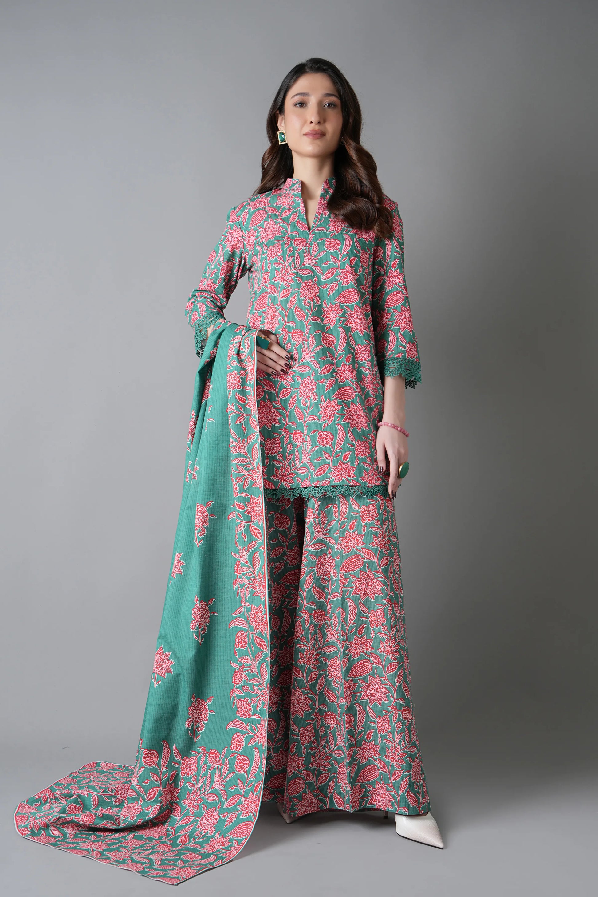 Woman wearing a floral outfit with a green dupatta against a gray background