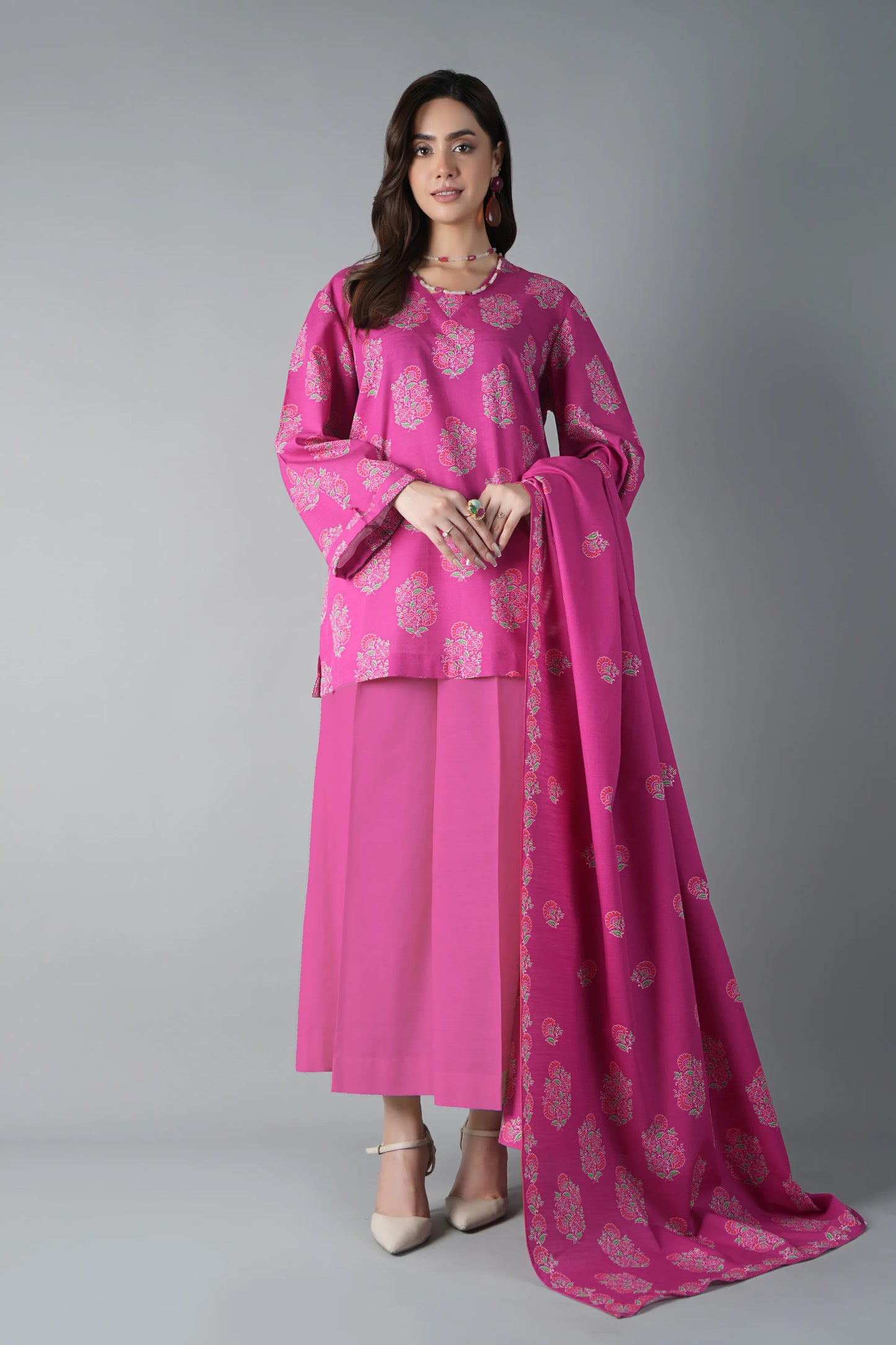 Woman wearing a pink traditional outfit with a matching dupatta on a gray background