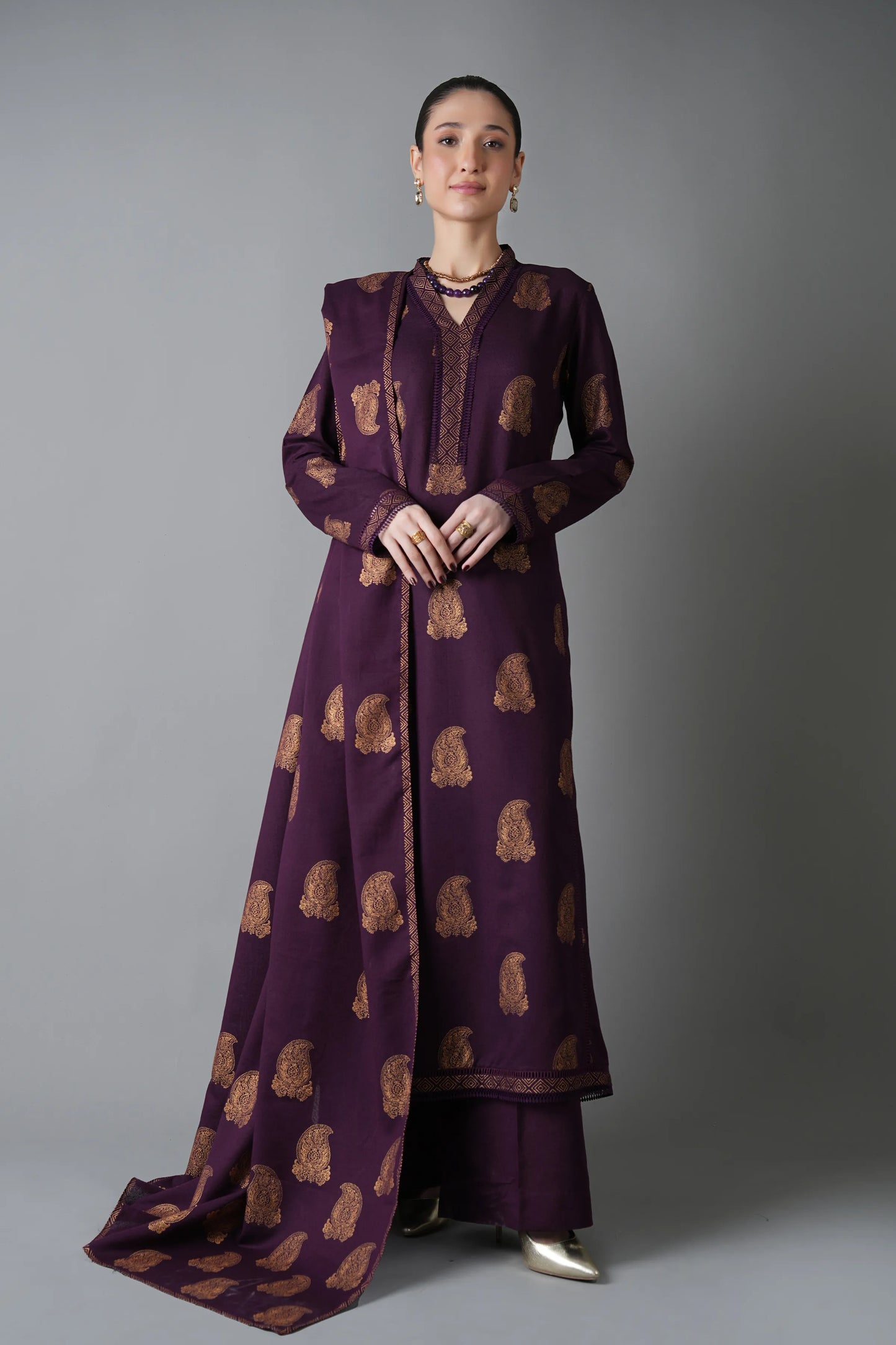 Woman wearing a long, dark purple dress with gold patterns against a gray background