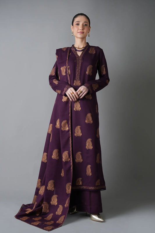 Woman wearing a long, dark purple dress with gold patterns against a gray background