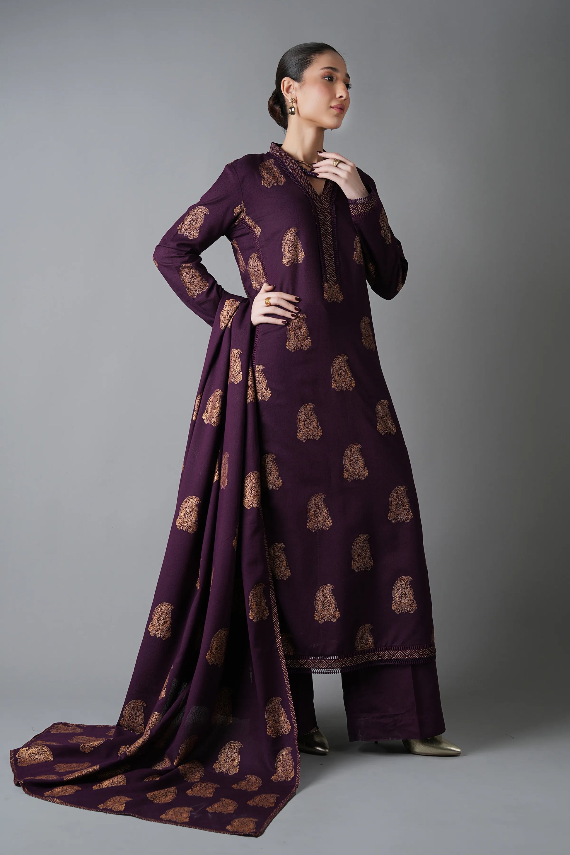 Woman wearing a long, dark purple dress with a pattern on a gray background