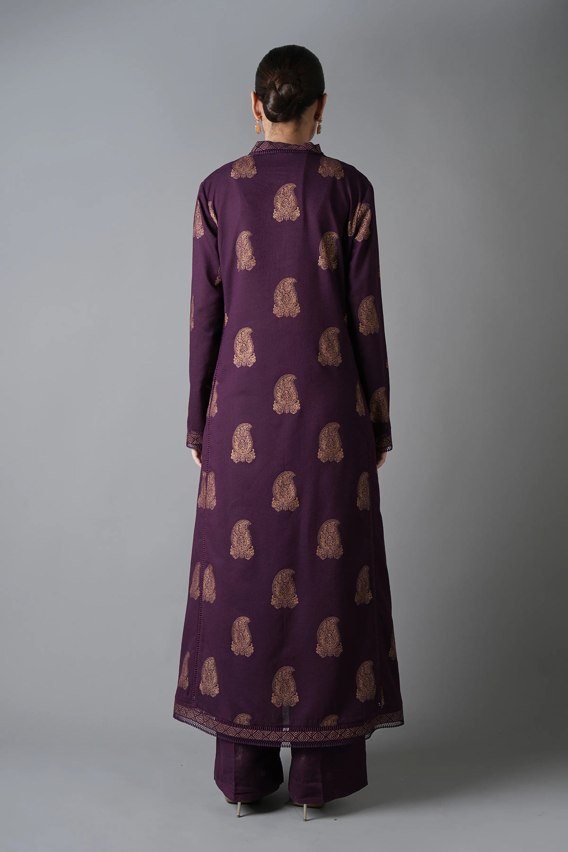 Person wearing a long purple dress with a pattern on a gray background