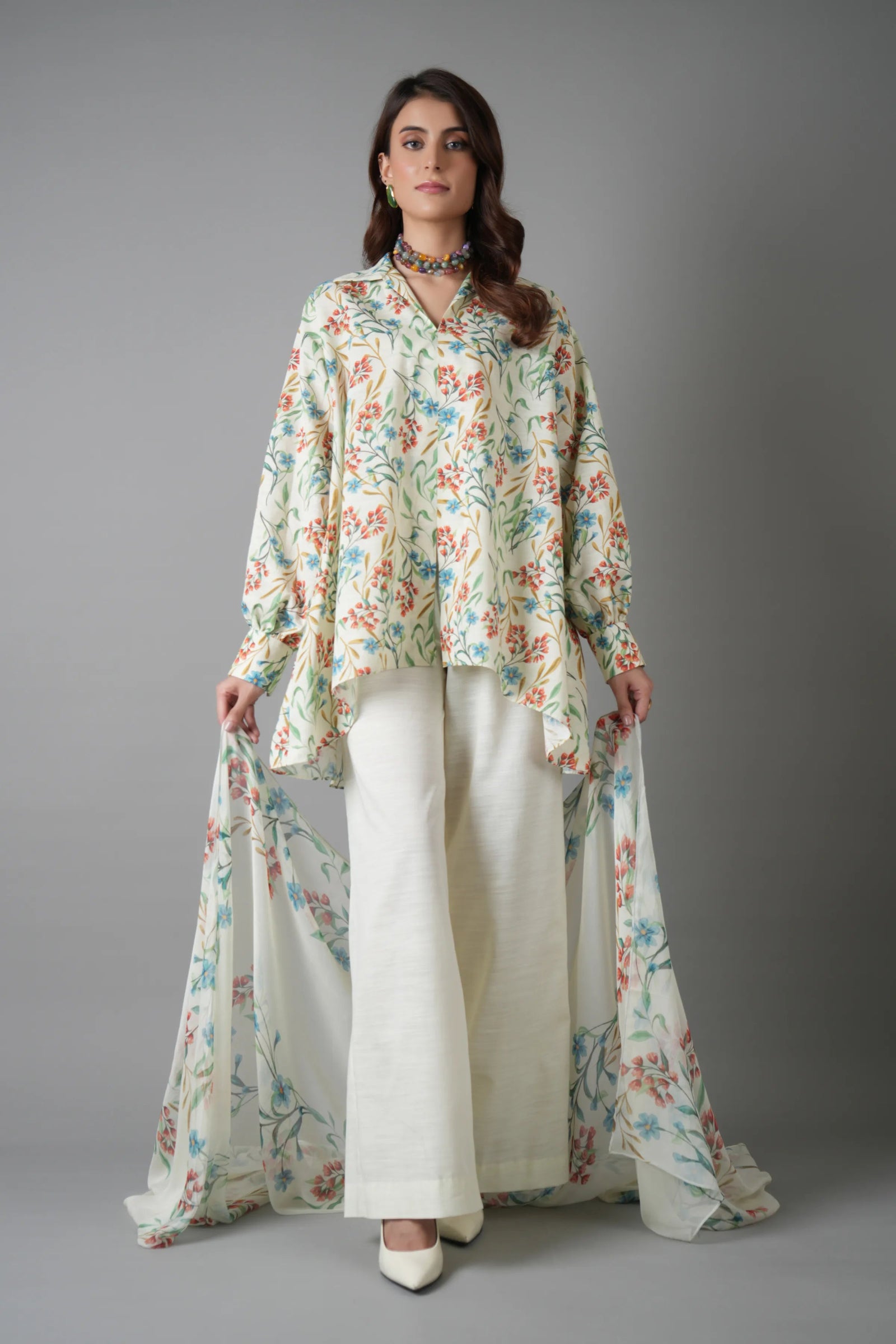 Woman wearing a floral top and white pants against a gray background