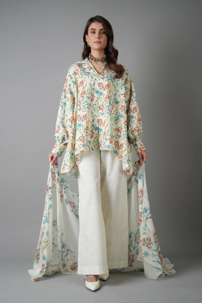 Woman wearing a floral top and white pants against a gray background