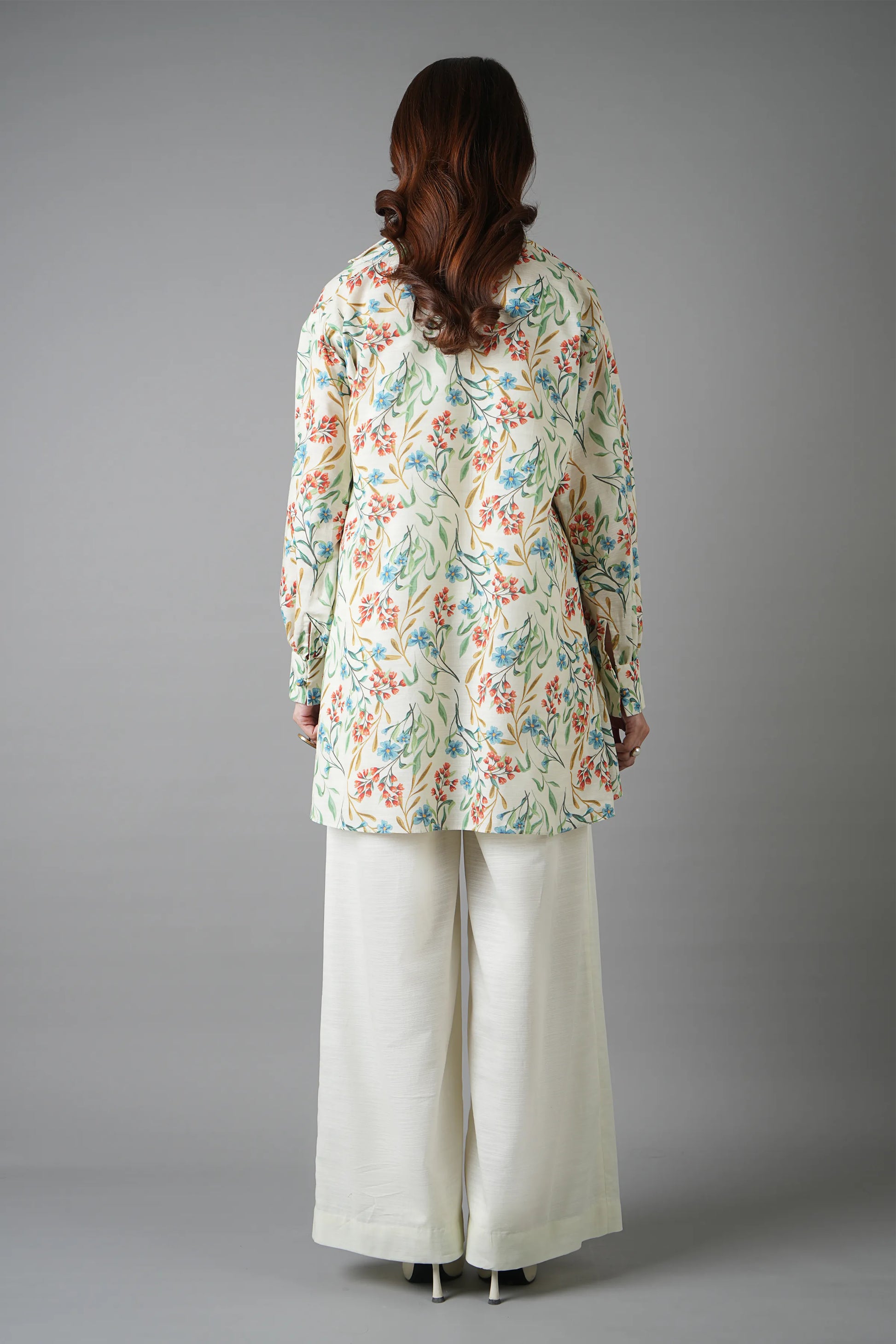 Person wearing a floral long-sleeve top and white pants on a gray background