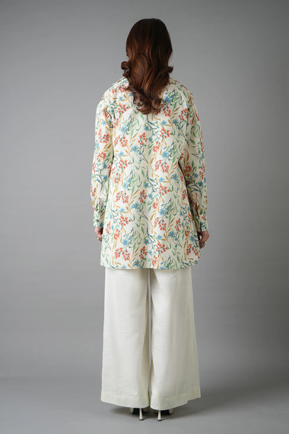 Person wearing a floral long-sleeve top and white pants on a gray background