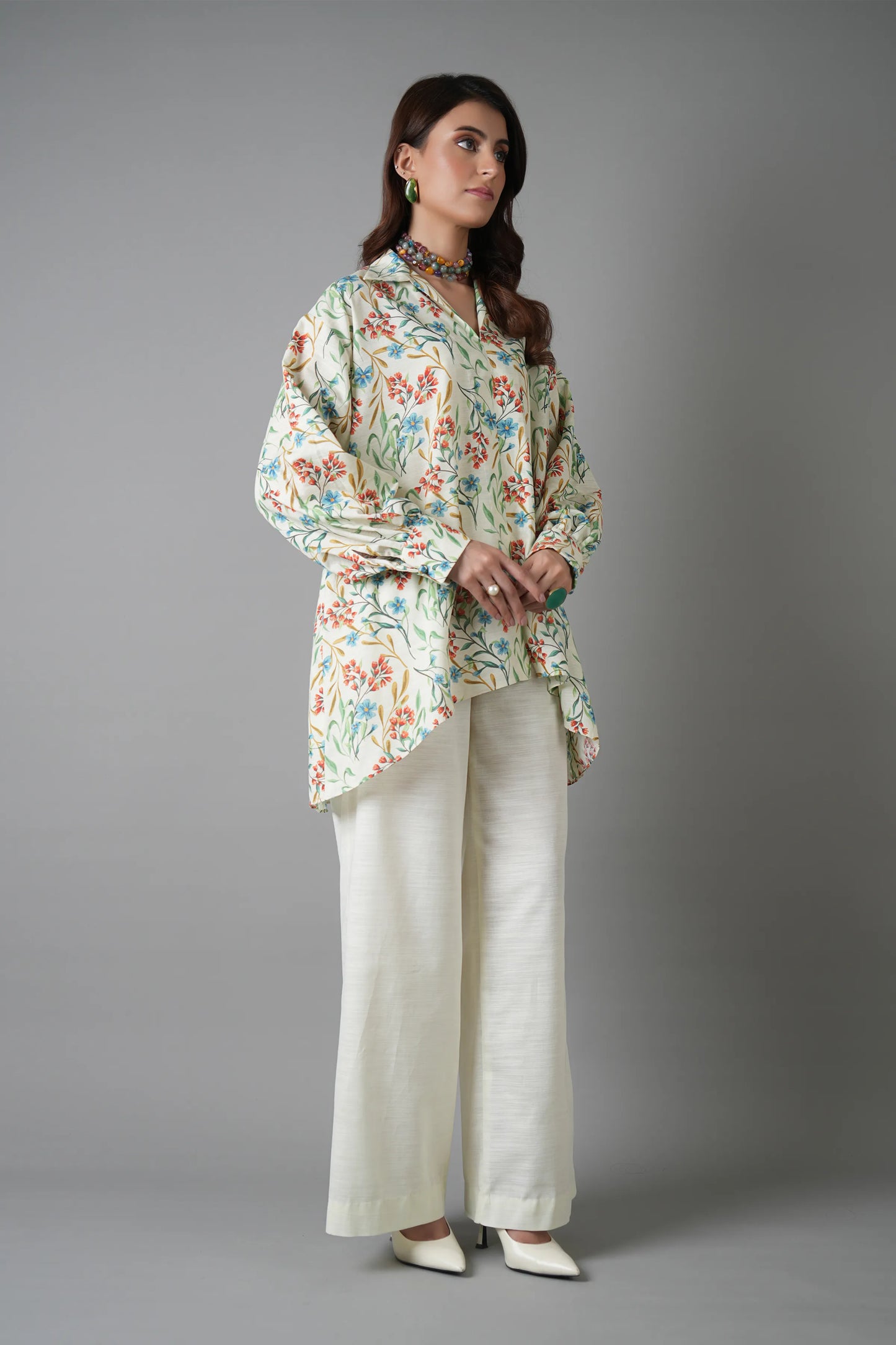 Woman wearing a floral blouse and white pants on a gray background