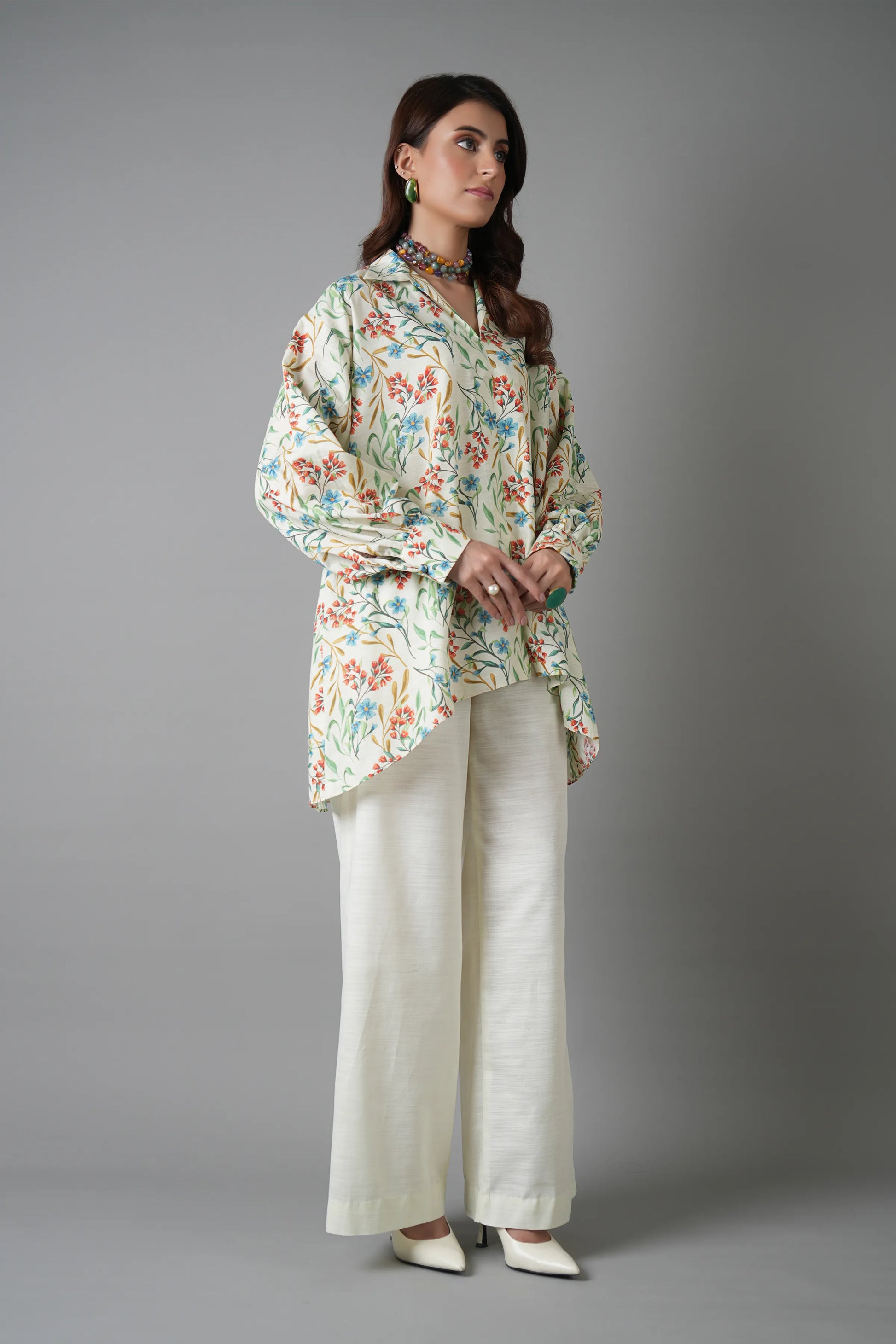 Woman wearing a floral blouse and white pants on a gray background