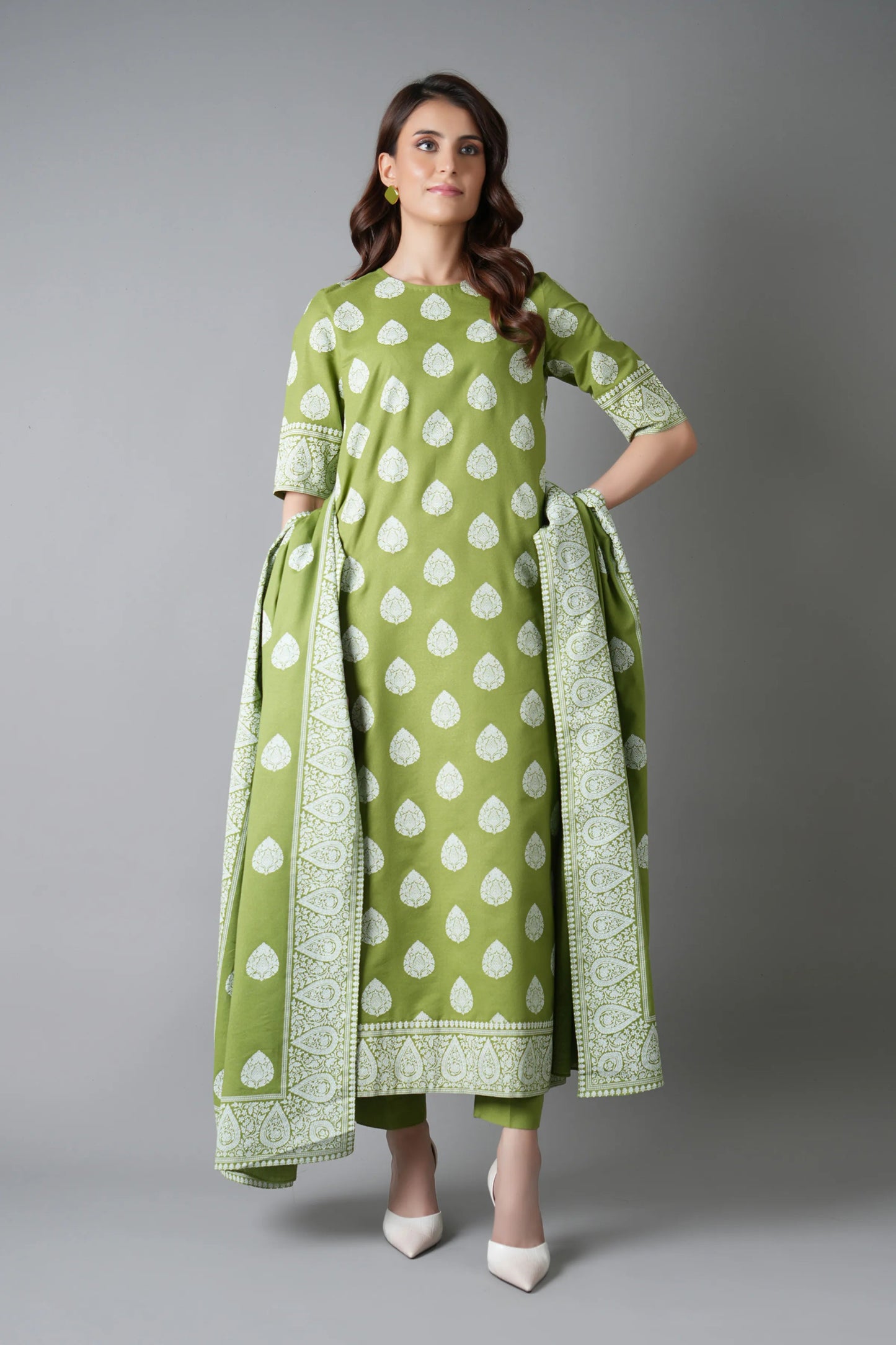 Woman wearing a green and white patterned outfit with a scarf on a gray background